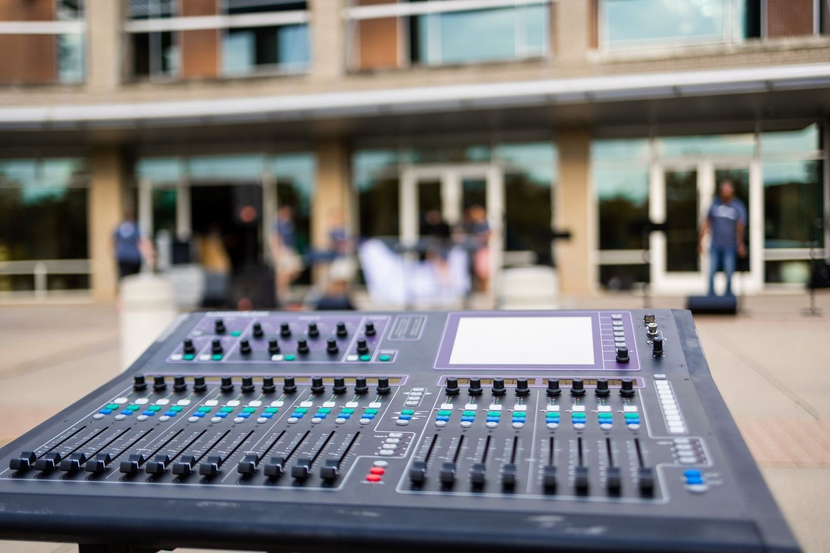 Digitales Mischpult vor einem unscharfen Live-Event-Aufbau